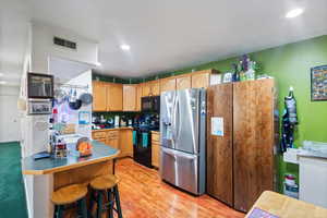 Kitchen with black appliances, a kitchen bar, light wood-style flooring, recessed lighting, and a peninsula