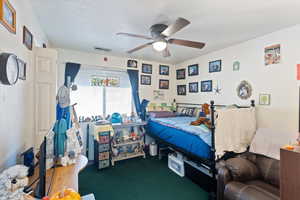 Carpeted bedroom with ceiling fan and a textured ceiling