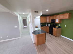 Kitchen featuring dark countertops, a peninsula, black appliances, recessed lighting, and wood finish cabinets