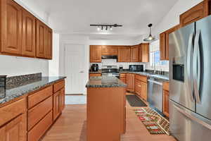 Kitchen featuring appliances with stainless steel finishes, brown cabinets, hanging light fixtures, dark stone counters, and light wood-style floors