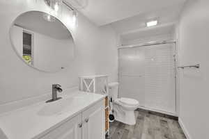 Bathroom with a textured ceiling, vanity, light wood-style flooring, and a shower stall