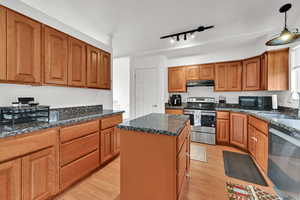 Kitchen featuring brown cabinets, black appliances, light wood-style flooring, dark stone countertops, and a center island