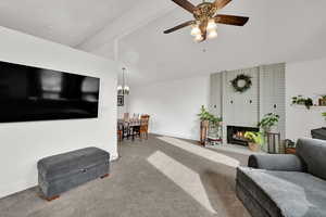 Carpeted living area featuring a brick fireplace, a chandelier, and ceiling fan