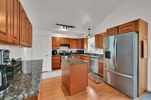 Kitchen featuring stainless steel appliances, brown cabinets, light wood-style flooring, dark stone counters, and a kitchen island