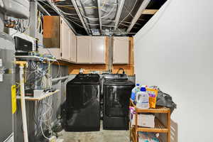 Laundry area featuring concrete flooring, gas water heater, washer and dryer, and cabinet space