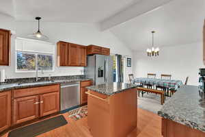 Kitchen featuring brown cabinets, hanging light fixtures, light wood-style flooring, a center island, and appliances with stainless steel finishes