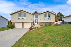 Split foyer home with brick siding, a front yard, driveway, and an attached garage