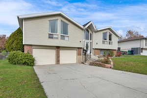 Split foyer home with a front lawn, brick siding, driveway, and an attached garage