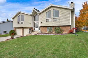 Bi-level home featuring brick siding, driveway, a chimney, and an attached garage