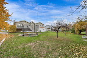 Back of house with a wooden deck, a lawn, a trampoline, an outbuilding, and a patio area