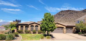 Mediterranean / spanish house with stone siding, a mountain view, a front lawn, stucco siding, and driveway