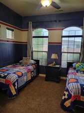 Bedroom with multiple windows, dark colored carpet, and a ceiling fan