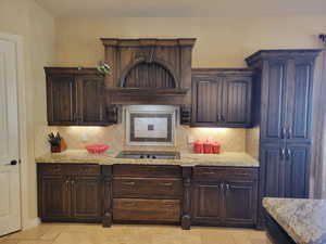 Kitchen with dark brown cabinets, decorative backsplash, premium range hood, and black electric stovetop