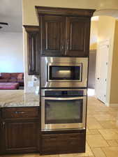 Kitchen featuring dark brown cabinetry, appliances with stainless steel finishes, stone tile floors, light stone counters, and backsplash