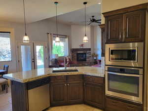 Kitchen with dark brown cabinets, appliances with stainless steel finishes, a stone fireplace, and open floor plan