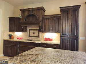 Kitchen with dark brown cabinets, tasteful backsplash, and light stone countertops