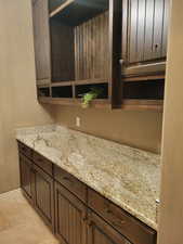 Kitchen with open shelves, dark brown cabinetry, and light stone counters