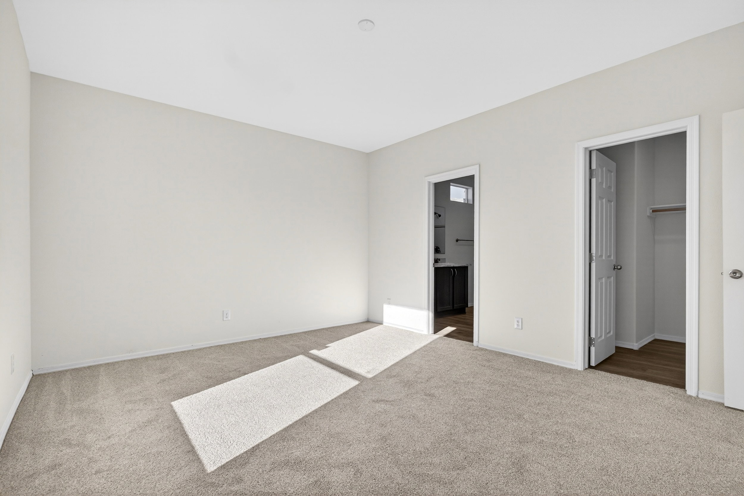 Unfurnished bedroom with light colored carpet, a spacious closet, and ensuite bath