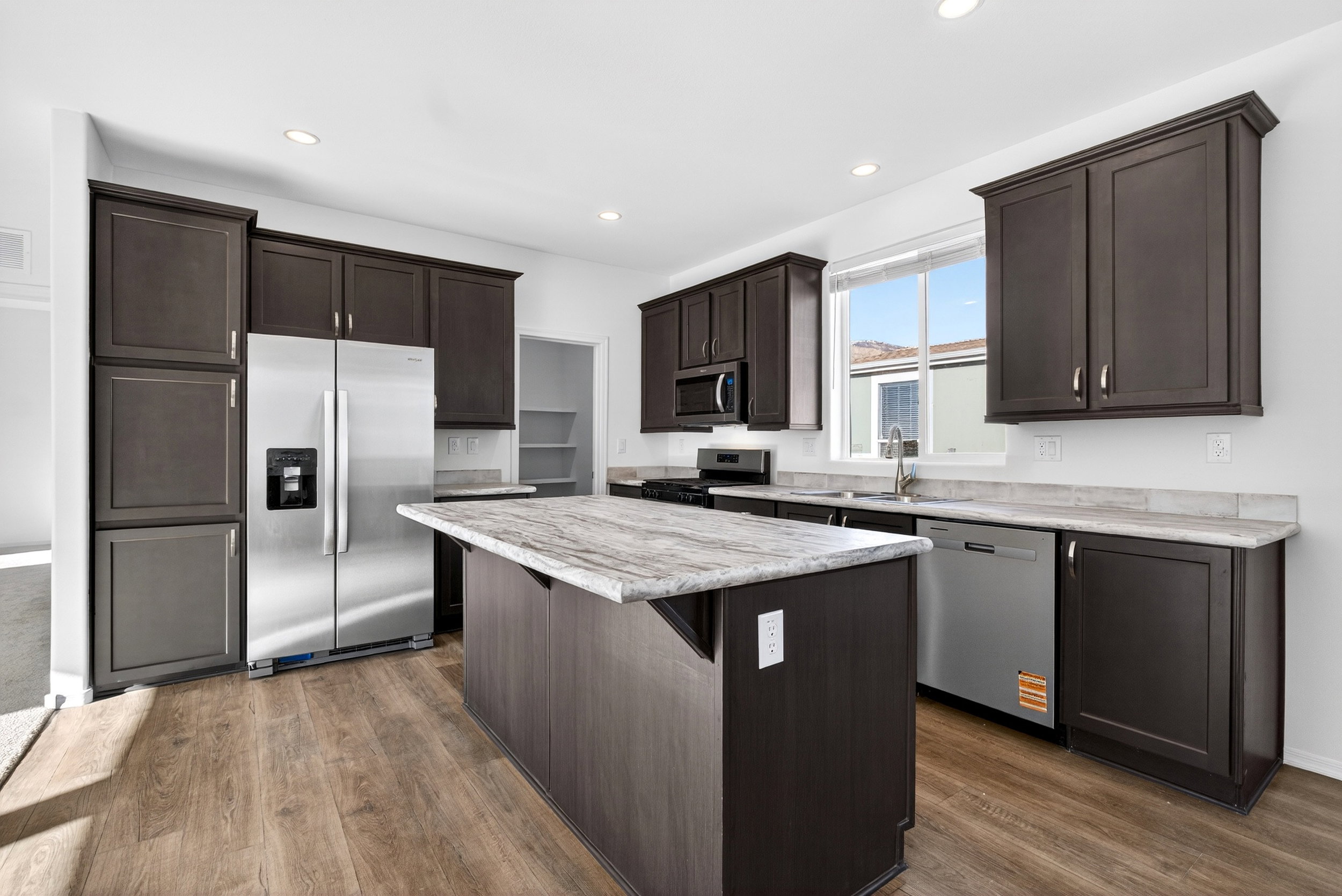 Kitchen with stainless steel appliances, dark wood finish cabinetry, a kitchen island, a breakfast bar area, and recessed lighting
