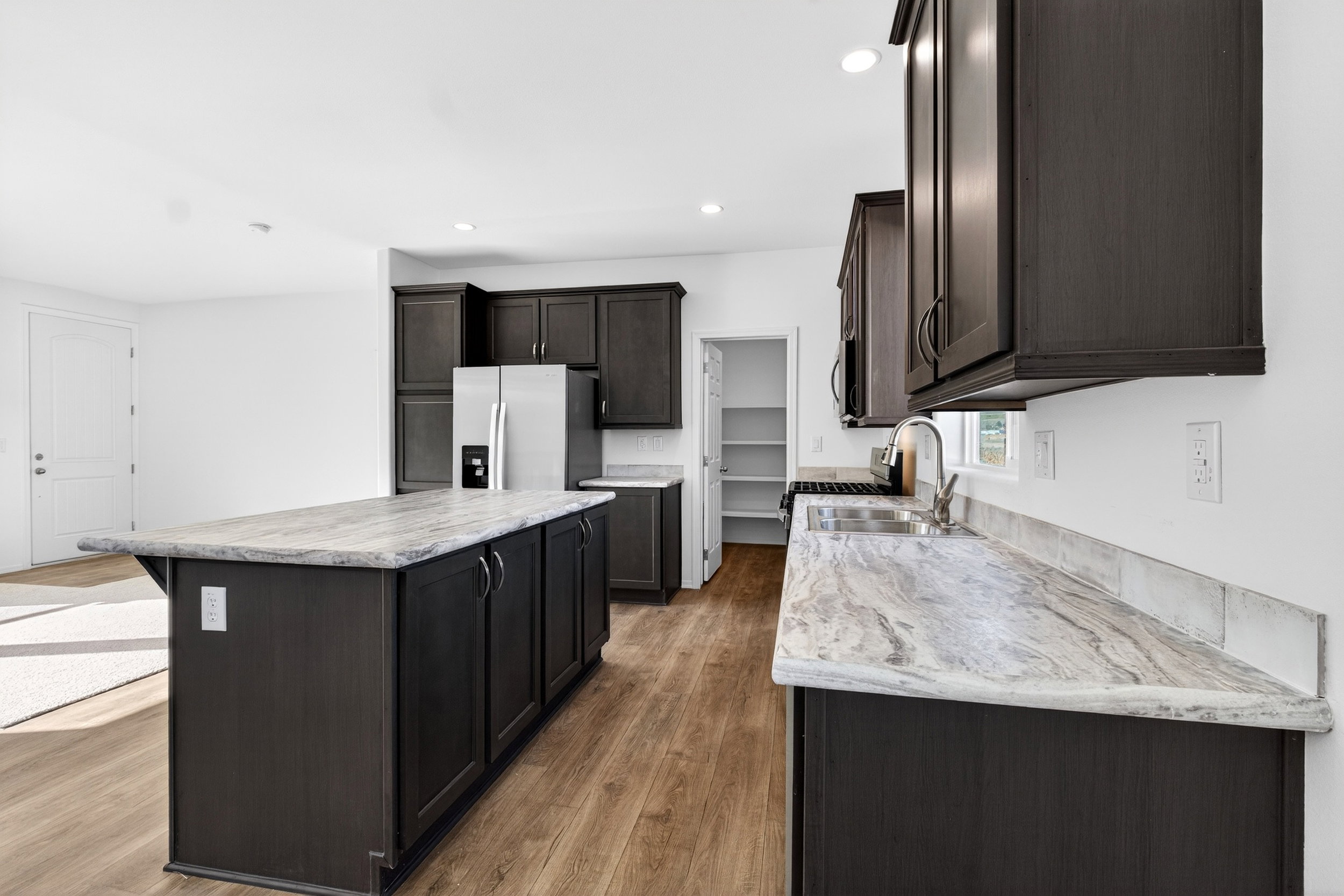 Kitchen featuring light countertops, stainless steel refrigerator with ice dispenser, dark wood finish cabinets, light wood finished floors, and a kitchen island