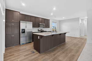 Kitchen with dark brown cabinetry, stainless steel appliances, light countertops, a breakfast bar, and a center island with sink