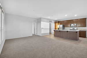 Kitchen featuring open floor plan, light carpet, a breakfast bar area, a kitchen island with sink, and stainless steel fridge with ice dispenser