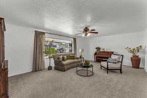 Living area with carpet floors, a ceiling fan, and a textured ceiling