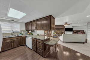 Kitchen with a fireplace, light stone countertops, dark brown cabinets, a breakfast bar, and dishwasher
