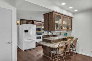 Kitchen featuring white appliances, light stone counters, glass insert cabinets, dark wood-style flooring, and recessed lighting