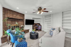 Living room with carpet flooring, a brick fireplace, ceiling fan, recessed lighting, and a textured ceiling