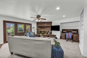 Carpeted living room featuring a textured ceiling, a brick fireplace, a ceiling fan, and recessed lighting