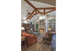 Living room with beam ceiling, high vaulted ceiling, dark wood-type flooring, a warm lit fireplace, and a ceiling fan
