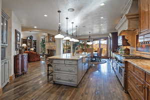 Kitchen with a kitchen breakfast bar, decorative light fixtures, a center island with sink, light stone counters, and double oven range