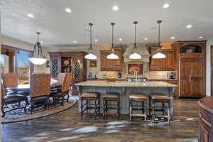Kitchen featuring brown cabinets, a breakfast bar, decorative light fixtures, a large island, and light stone counters