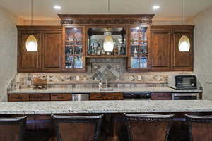 Kitchen featuring a breakfast bar area, light stone countertops, decorative backsplash, and a textured wall
