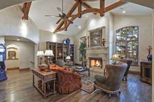 Living area featuring arched walkways, hardwood / wood-style flooring, high vaulted ceiling, beam ceiling, and ceiling fan