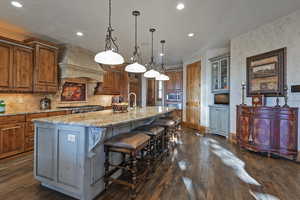 Kitchen with a kitchen bar, backsplash, a large island, hanging light fixtures, and light stone counters