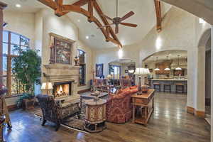 Living area with arched walkways, high vaulted ceiling, dark wood-style floors, ceiling fan, and beamed ceiling