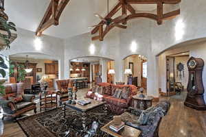Living room featuring dark wood finished floors, beamed ceiling, ceiling fan, high vaulted ceiling, and arched walkways