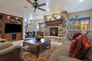 Living room with healthy amount of natural light, a stone fireplace, a ceiling fan, and light carpet