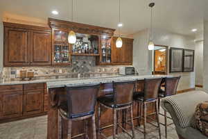 Indoor wet bar with light stone countertops, pendant lighting, decorative backsplash, and recessed lighting