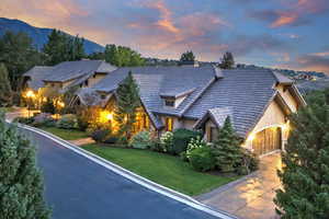 View of front facade featuring a chimney, stucco siding, stone siding, and a lawn