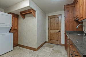 Washroom featuring cabinet space, stacked washer and clothes dryer, a textured ceiling, and light tile patterned floors