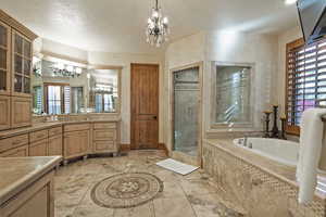 Bathroom with vanity, a garden tub, a shower stall, a chandelier, and a textured ceiling