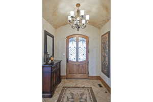 Foyer with lofted ceiling, a chandelier, french doors, light tile patterned flooring, and arched walkways