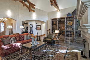 Living area featuring a ceiling fan, arched walkways, dark wood-style floors, a chandelier, and a towering ceiling