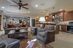 Living room featuring arched walkways, wine cooler, light carpet, a ceiling fan, and recessed lighting