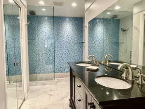 Full bathroom with a shower stall, double vanity, light marble finish flooring, recessed lighting, and tile walls