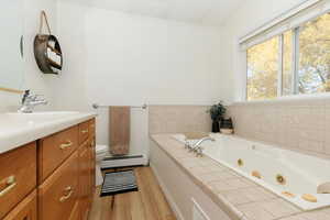 Bathroom featuring vanity, a tub with jets, baseboard heating, and light wood finished floors
