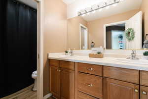 Full bath with double vanity, light wood-style flooring, and curtained shower